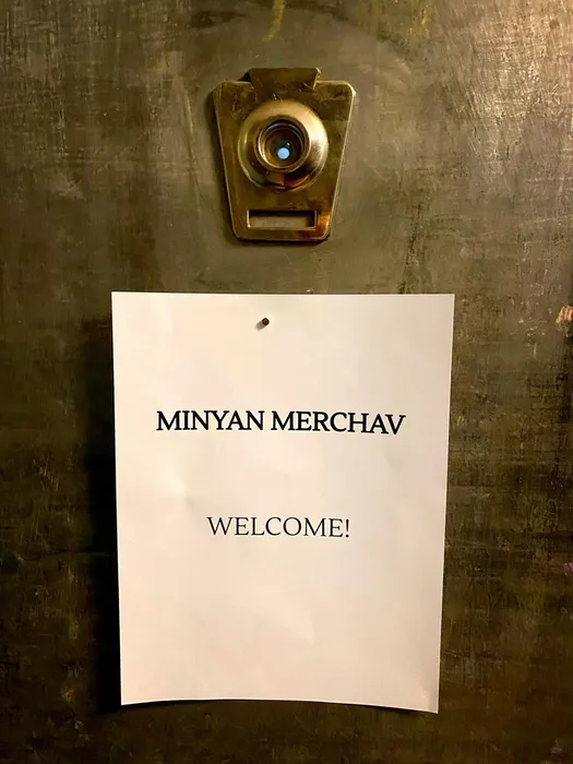 An image of an open door with a sign reading "Minyan Merchav - Welcome!"